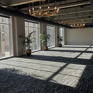 The inside of the LaFayette room in the Cambria Hotel. There are large glass windows allowing natural light into the carpeted room, and grand chandeliers hanging from the ceiling