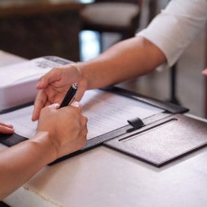 A woman signs a contract while another woman points to a specific part in the contract.