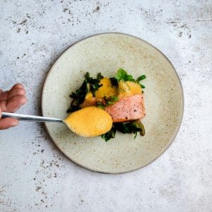 Chef preparing a special meal for an event Chef adding sauce to a salmon entrée before serving at an event.