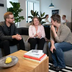 Budget-Friendly Employee Appreciation Ideas Three coworkers smiling and talking around a coffee table during a team meeting.